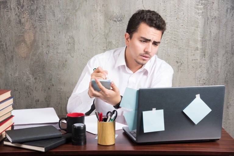 Office employee looking at laptop and holding telephone at the office desk